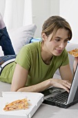 Young woman eating pizza while working at computer