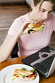 Young woman eating sandwich while working at computer