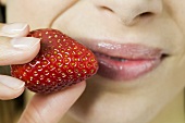 Young woman holding fresh strawberry in front of her mouth