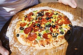 Hands holding pepperoni pizza with peppers and olives