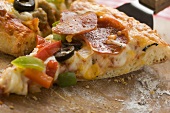 Stück Pizza mit Peperoniwurst, Paprika und Oliven auf Heber
