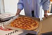 Man holding pizza box containing pepperoni pizza