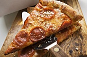 Two pieces of pepperoni pizza with server on wooden board