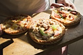 Person holding wooden board with three different mini-pizzas