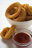 Deep-fried onion rings in white bowl, ketchup
