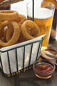 Deep-fried onion rings in wire basket, ketchup, beer, salt
