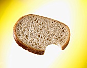 Slice of bread with bite taken against yellow background