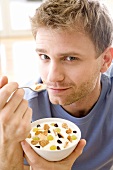 Junger Mann isst Joghurt-Beeren-Müsli