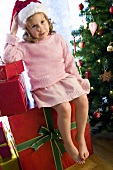 Girl in Father Christmas hat sitting on Christmas gift