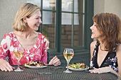 Two women with salad and wine at table on a terrace