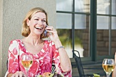 Blond woman on phone sitting at laid table on a terrace
