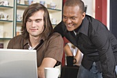 Zwei Männer im Café blicken interressiert auf einen Laptop