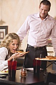 Woman in restaurant eating pizza, man just arriving