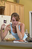 Young woman eating fruit-flavoured cereal loops, reading newspaper