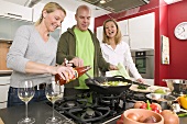 Mann und zwei Frauen kochen gemeinsam ein Wokgericht