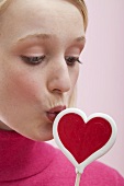 Young woman kissing a heart-shaped lollipop