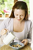 Young woman pouring milk over cornflakes