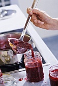 Raspberry jam being ladled into a screw-top jar