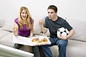 Young couple with pizza & football sitting in front of TV