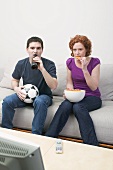 Junges Paar mit Fussball, Bierflasche & Chips beim Fernsehen