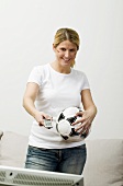 Young woman with football & remote standing in front of TV