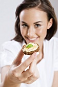 Young woman holding pumpernickel canapé towards camera