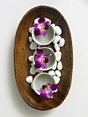 Flowers in small bowls and pebbles in wooden dish