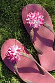 Rosa Flip-Flops mit Blüte im Gras