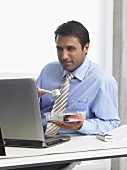 Businessman eating sushi while looking at his laptop