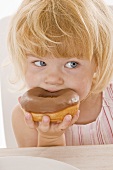 Kleines Mädchen isst Doughnut mit Schokoglasur