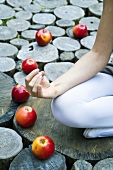 Junge Frau sitzt auf Baumstamm umgeben von Äpfeln