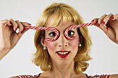 Blond woman holding candy canes in front of her eyes