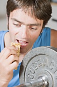 Man eating muesli bar on weight bench