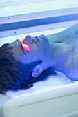 Young man in tanning goggles lying on tanning bed