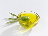 A green olive in a small glass dish of olive oil