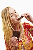A young woman biting a piece of dark chocolate