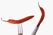 Two red chili peppers speared on knife and fork