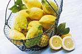 Bio-Zitronen in einem Drahtkorb, davor eine halbierte Zitrone