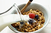 Pouring milk over crunchy muesli with berries in bowl
