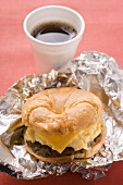 Cheeseburger with scrambled egg on aluminium foil, coffee cup