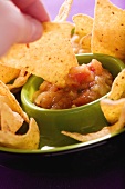 Tortilla chip being dipped in tomato salsa