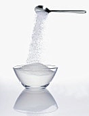 Sugar trickling from a spoon into a small bowl