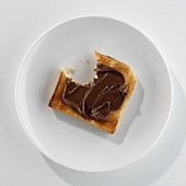 Eine Scheibe angebissener Toast mit Nutella auf einem Teller