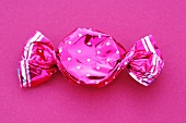 A sweet in a pink wrapper on a pink background