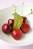 Five cherries with leaf in a small bowl