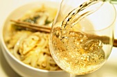 Pouring a glass of wine, noodle dish in background