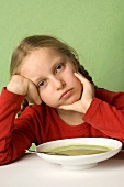 Girl sitting listlessly in front of plate of vegetable soup