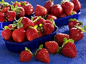 Three punnets of strawberries with strawberries beside them