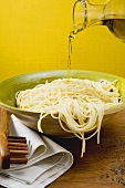 Pouring olive oil over cooked spaghetti