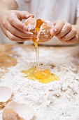 Child breaking an egg onto a heap of flour